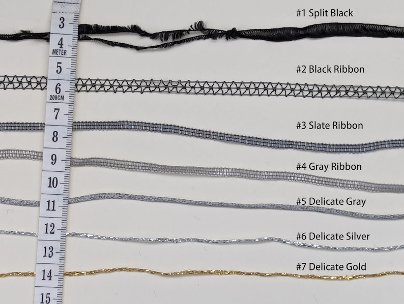 May include: Seven different types of ribbon, including split black, black ribbon, slate ribbon, gray ribbon, delicate gray, delicate silver, and delicate gold. The ribbons are laid out horizontally on a white surface with a ruler in the left side of the image.