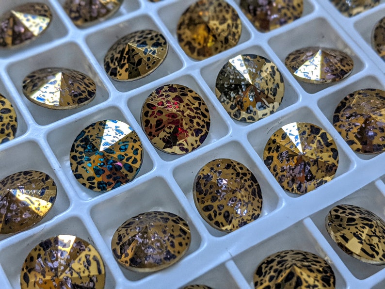 May include: A close-up of a tray of round, faceted rhinestones with a leopard print pattern. The rhinestones are in various colors, including gold, red, and blue.