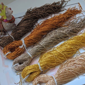 May include: Five spools of metallic thread in various shades of gold, brown, and beige. The thread is arranged in a fan shape on a white surface.