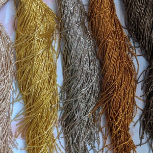 May include: Five spools of seed beads in different metallic colors: gold, silver, rose gold, copper, and gunmetal. The beads are very small and are arranged in a row.