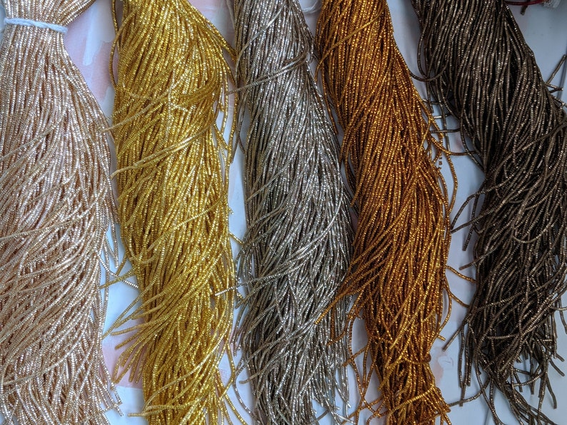 May include: Five spools of seed beads in different metallic colors: gold, silver, rose gold, copper, and gunmetal. The beads are very small and are arranged in a row.