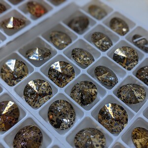 May include: A close-up of a tray of round, gold-toned rhinestones with a leopard print design. The rhinestones are arranged in a grid pattern.