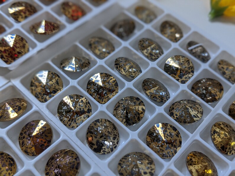 May include: A close-up of a tray of round, gold-toned rhinestones with a leopard print design. The rhinestones are arranged in a grid pattern.