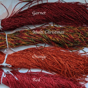 May include: Four spools of metallic seed beads in various colors: garnet, multi-Christmas, orange, and red. The spools are labeled with the color names.