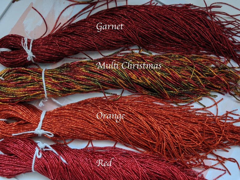 May include: Four spools of metallic seed beads in various colors: garnet, multi-Christmas, orange, and red. The spools are labeled with the color names.