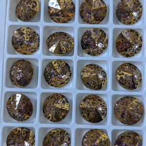May include: A close-up view of a grid of small, round, decorative, gold-toned, glass rhinestones with a leopard print pattern. The rhinestones are arranged in rows and columns.