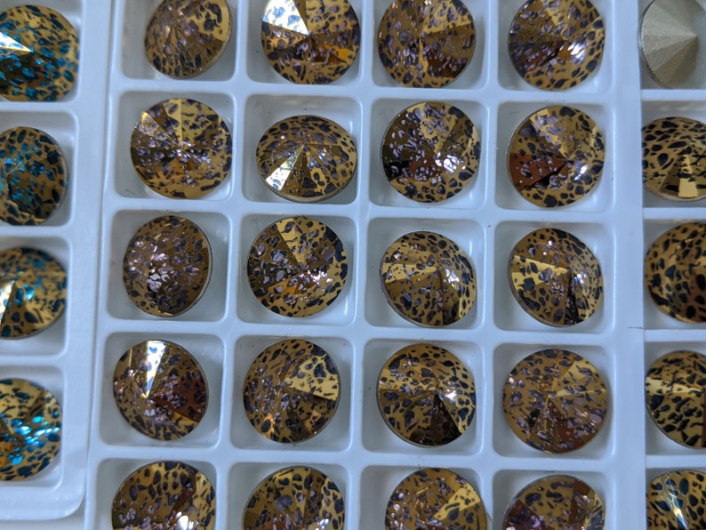 May include: A close-up view of a grid of small, round, decorative, gold-toned, glass rhinestones with a leopard print pattern. The rhinestones are arranged in rows and columns.