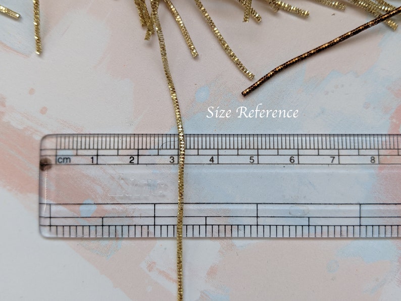 May include: A gold chain measuring 5 cm in length, next to a ruler for size reference.  The chain is made of small, linked squares.