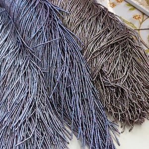 May include: Two bundles of iridescent metallic fringe, one in a light blue-purple shade and the other in a darker gray-purple shade. The fringe is made of thin, shiny strands.