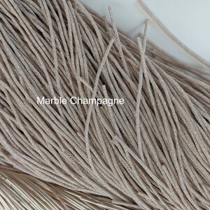 May include: A close-up of a bundle of thin, shimmery, beige-colored cords. The cords are arranged in a random pattern and have a subtle sparkle. The text "Marble Champagne" is visible in the image.