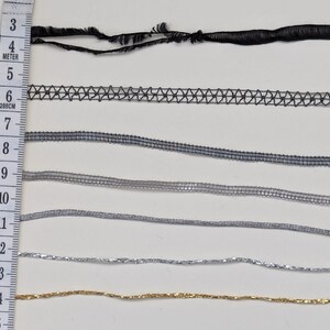 May include: A close-up of eight different types of trim, including black, gray, and silver. The trim is arranged in rows and measured with a ruler in inches.