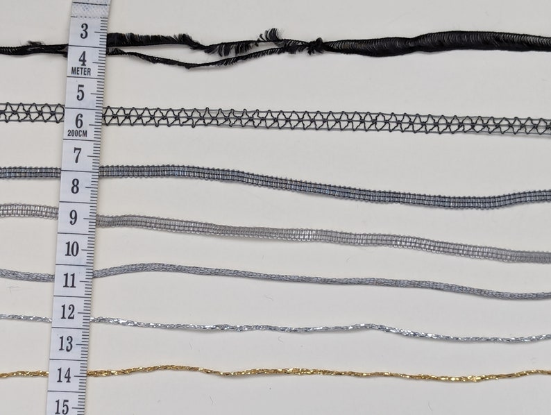 May include: A close-up of eight different types of trim, including black, gray, and silver. The trim is arranged in rows and measured with a ruler in inches.