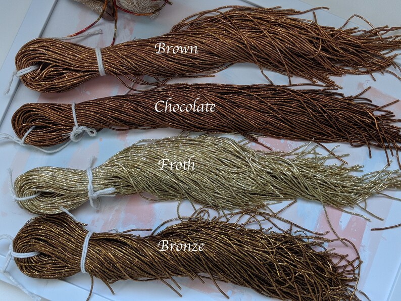 May include: Four spools of metallic seed beads in different colors: brown, chocolate, froth, and bronze. The beads are arranged in rows on a white surface.