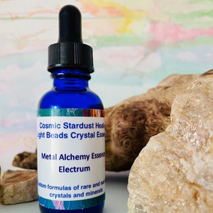May include: A blue glass bottle with a dropper top and a white label that reads "Cosmic Stardust Healing Light Beads Crystal Essence Metal Alchemy Essence Electrum Custom formulas of rare and natural crystals and minerals".