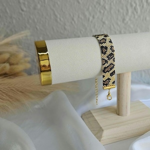May include: A gold bracelet with a leopard print pattern on a white display stand. The bracelet has a gold clasp.