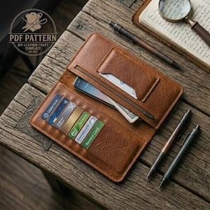 May include: Open brown leather wallet with multiple card slots, a zippered pocket, and a compartment for a smartphone. The wallet is on a wooden surface with pens, a notebook, and a magnifying glass. The text "PDF PATTERN DIY LEATHER CRAFT TEMPLATE" is visible.