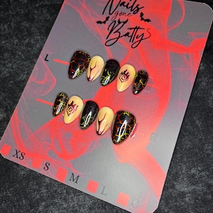 May include: A set of press-on nails in various sizes, displayed on a gray and red card. The nails feature black and yellow crackle designs, cream-colored accents, and a logo. The card reads "Nails gone Batty".