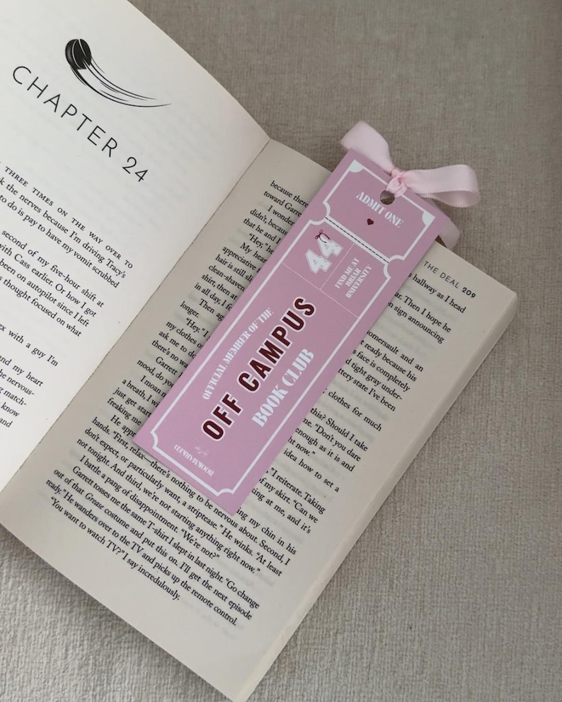 May include: A pink bookmark with the text "OFF CAMPUS BOOK CLUB" and "ADMIT ONE" is placed in an open book. The bookmark has a pink ribbon tied at the top. The book is open to Chapter 24.