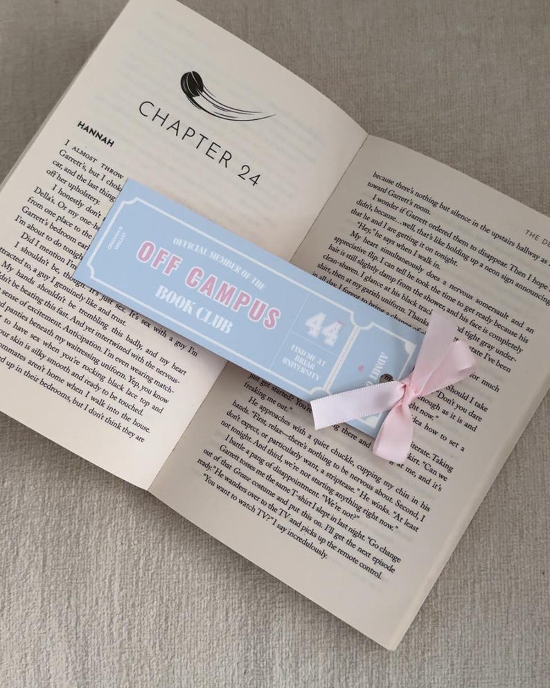 May include: Open book with a light blue bookmark that reads "OFF CAMPUS BOOK CLUB" in pink text. A pink ribbon is attached to the bookmark. The book is open to Chapter 24.
