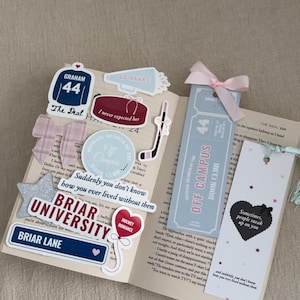 Op de afbeelding: Een open boek met diverse stickers en bladwijzers. Stickers tonen zinnen als "Briar University" en "Hockey Romance". Bladwijzers zijn versierd met roze linten en de tekst "Off Campus Book Club".