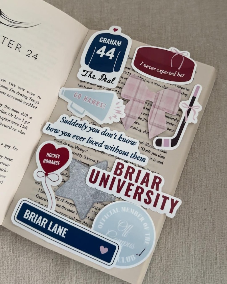May include: A collection of stickers on an open book. Stickers include a hockey jersey with "GRAHAM 44", a hockey puck, a hockey stick, and text that reads "BRIAR UNIVERSITY" and "BRIAR LANE". The stickers are in shades of blue, burgundy, and white.