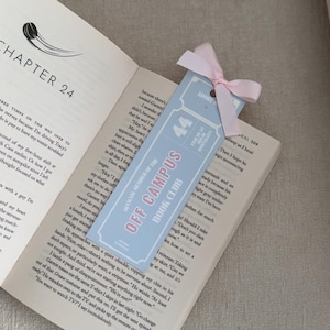 May include: A light blue bookmark with the text "OFF CAMPUS BOOK CLUB" and "44" in pink. The bookmark is tied with a pink ribbon and is placed in an open book.