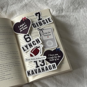 May include: A collection of stickers on an open book. The stickers feature text like "I think I need you for keeps," "6 LYNCH," and "13 KAVANAGH." Other stickers include a football and an iPod.