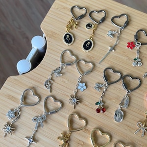 Peut inclure: Une collection de porte-clés en forme de cœur avec divers breloques en métal, notamment des épées miniatures, des fleurs, des nœuds, des étoiles, des cerises, des papillons, des lunes et des cadres ovales avec des roses noires, en métal argenté et doré.