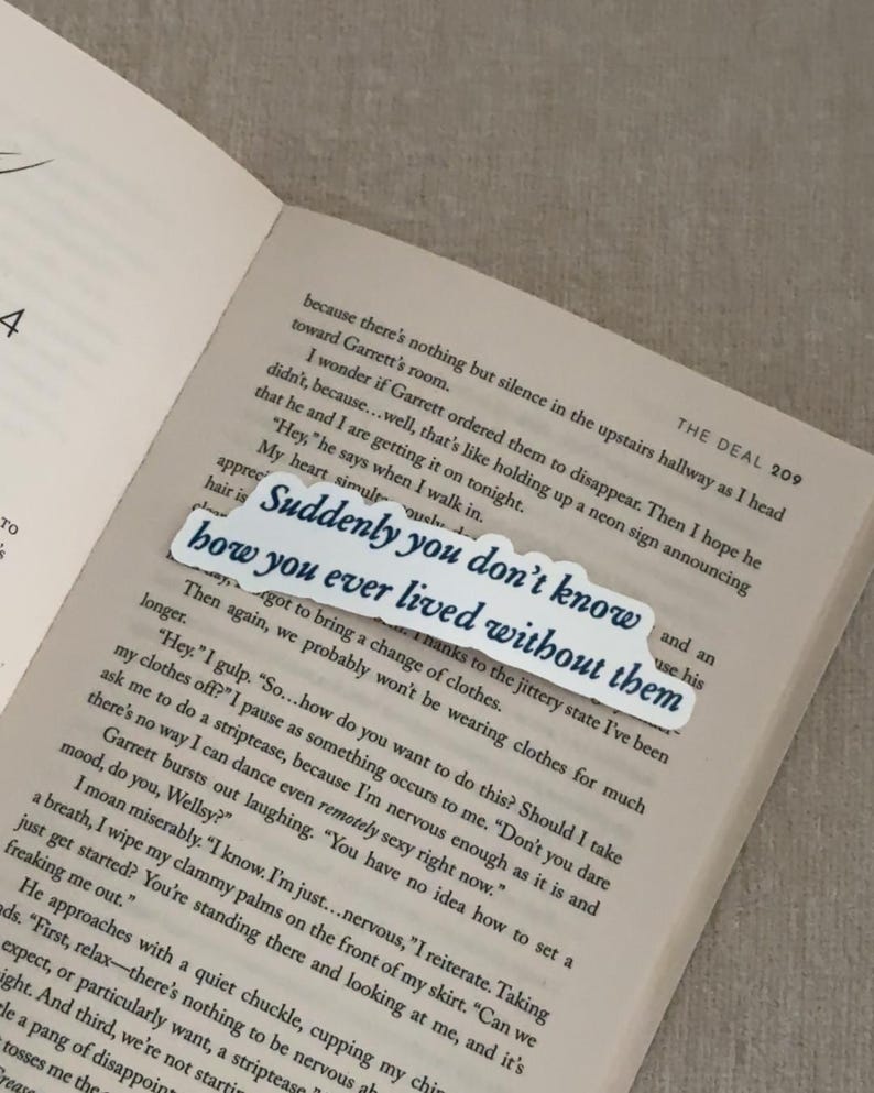 May include: A white bookmark with the text "Suddenly you don't know how you ever lived without them" in a dark blue font, placed on an open book. The book's pages are light beige.