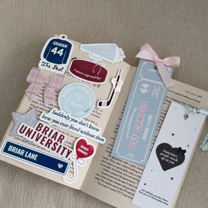 May include: An open book with various stickers and bookmarks. Stickers include a hockey jersey, a megaphone, and a hockey puck. Bookmarks feature a ticket design and a heart with text. A pink bow adorns one bookmark.