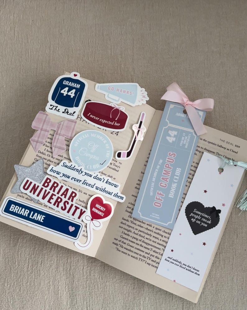 May include: An open book with various stickers and bookmarks. Stickers include a hockey jersey, a megaphone, and a hockey puck. Bookmarks feature a ticket design and a heart with text. A pink bow adorns one bookmark.