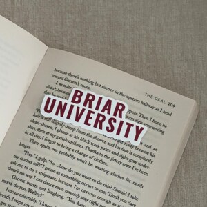 May include: A white sticker with the text "BRIAR UNIVERSITY" in maroon letters is placed on an open book. The book's pages are filled with printed text. The sticker is rectangular with a white border.