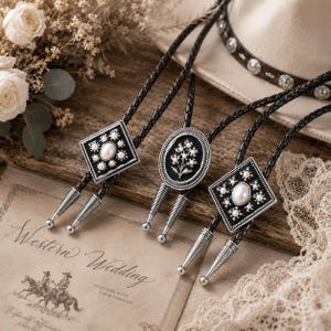 May include: Three bolo ties with black braided cords and decorative silver-toned slides. The bolo tie pendants feature geometric and floral designs with faux pearl accents. A Western Wedding invitation is visible in the background.