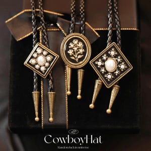 May include: Three bolo ties with black braided cords and decorative gold-toned pendants. The pendants feature geometric and floral designs with faux pearls. The bottom of each tie has a gold-toned cone-shaped accent. The text "CowboyHat" is visible at the bottom.