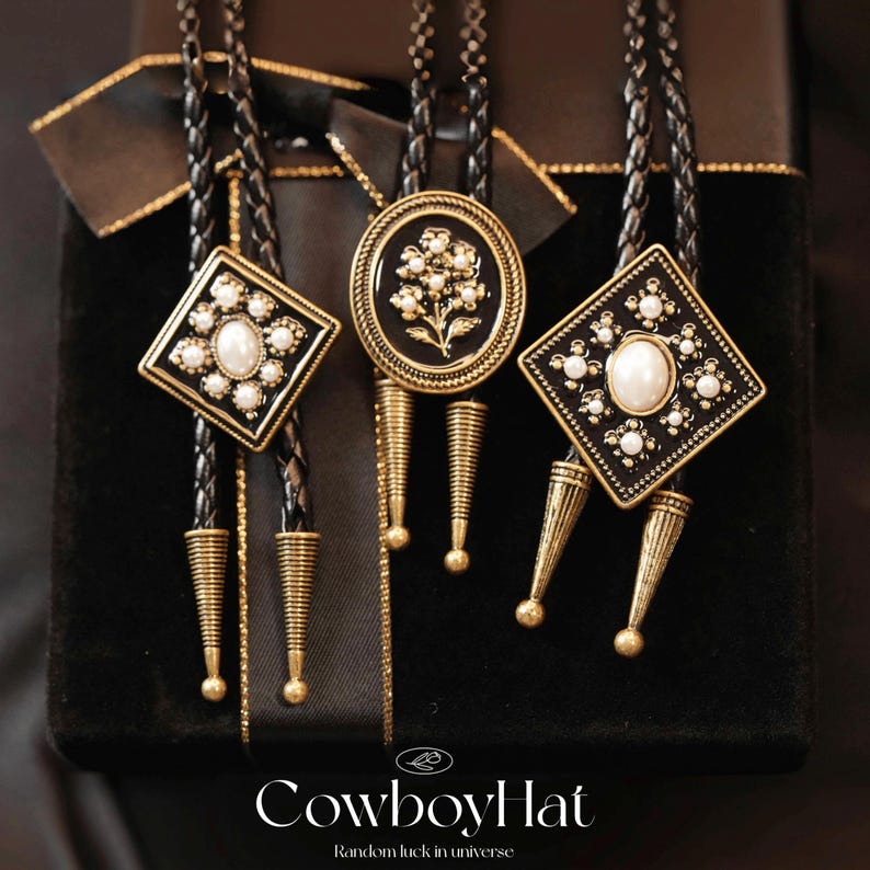 May include: Three bolo ties with black braided cords and decorative gold-toned pendants. The pendants feature geometric and floral designs with faux pearls. The bottom of each tie has a gold-toned cone-shaped accent. The text "CowboyHat" is visible at the bottom.