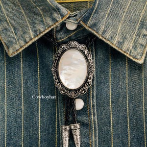 May include: An oval bolo tie with a mother-of-pearl center and ornate silver-tone frame. The tie is on a denim shirt with white pinstripes. The text "Cowboyhat" is visible at the bottom left.