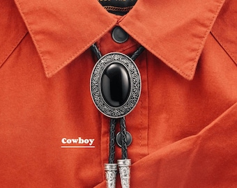 May include: An orange button-down shirt with a black bolo tie. The bolo tie has a black oval stone set in an ornate silver-colored frame. The shirt's label reads "Howler B.R.O." and the word "cowboy" is printed on the shirt.