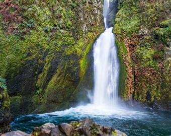 Könnte beinhalten: Ein Wasserfall stürzt über mit Moos bewachsenen Felsen und erzeugt eine ruhige und malerische Szenerie.