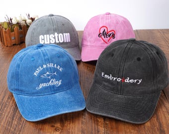 May include: Four baseball caps in various colors are displayed. One is gray with "custom" embroidered in white, another is pink with a heart and "Mom", a blue cap with "PAUL & SHARK yachting", and a black cap with "Embroidery".