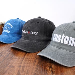 Pu&ograve; includere: Tre cappellini da baseball in blu, nero e grigio. Il cappellino blu presenta la scritta bianca Shark Yachting. Il cappellino nero ha la scritta bianca embroidery con una o rossa. Il cappellino grigio presenta la scritta bianca custom in stampatello.