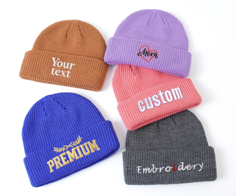 May include: A collection of colorful knit beanies. The beanies are in shades of brown, purple, pink, gray, and blue. Each beanie has embroidered text, including "Your text", "Mom", "Custom", "Premium", and "Embroidery".