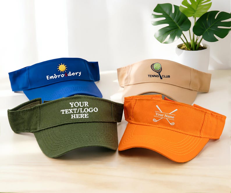 K&ouml;nnte beinhalten: Vier Sonnenblenden in Blau, Beige, Gr&uuml;n und Orange. Die blaue Sonnenblende hat eine Sonne und das Wort "Embroidery". Die beige Sonnenblende hat einen Tennisball und einen Schl&auml;ger mit "Tennis Club". Die gr&uuml;ne Sonnenblende sagt "YOUR TEXT/LOGO HERE". Die orangefarbene Sonnenblende hat gekreuzte Golfschl&auml;ger und "Your Name".
