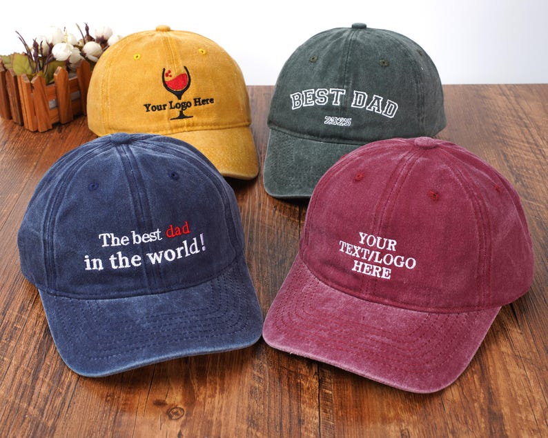 Pu&ograve; includere: Quattro cappellini da baseball in giallo, verde scuro, blu navy e bordeaux. Il cappellino giallo presenta un grafico di un calice di vino e del testo. Quello verde scuro dice BEST DAD 2025. Quello blu navy dice The best dad in the world! Quello bordeaux dice YOUR TEXT/LOGO HERE.
