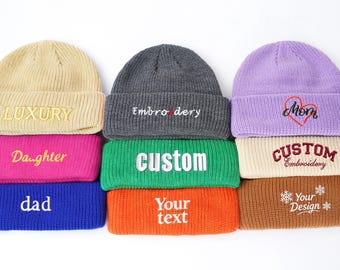 May include: A collection of colorful knit beanies with embroidered text. Colors include tan, pink, blue, gray, green, orange, and brown. Text includes "LUXURY", "Daughter", "dad", "Embroidery", "custom", "Your text", "Mom", "Custom Embroidery", and "Your Design".