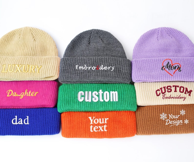 May include: A collection of colorful knit beanies with embroidered text. The beanies are in various colors, including tan, gray, purple, pink, green, blue, and orange. The text includes "LUXURY", "Embroidery", "Mom", "Daughter", "CUSTOM", "dad", and "Your text".