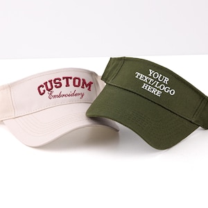 K&ouml;nnte beinhalten: Zwei Sonnenblenden, eine beige und eine olivgr&uuml;ne, werden gezeigt. Die beige Sonnenblende hat die Stickerei "CUSTOM Embroidery" in Burgunderrot. Die gr&uuml;ne Sonnenblende hat "YOUR TEXT/LOGO HERE" in Wei&szlig;. Beide Sonnenblenden sind auf wei&szlig;em Hintergrund.