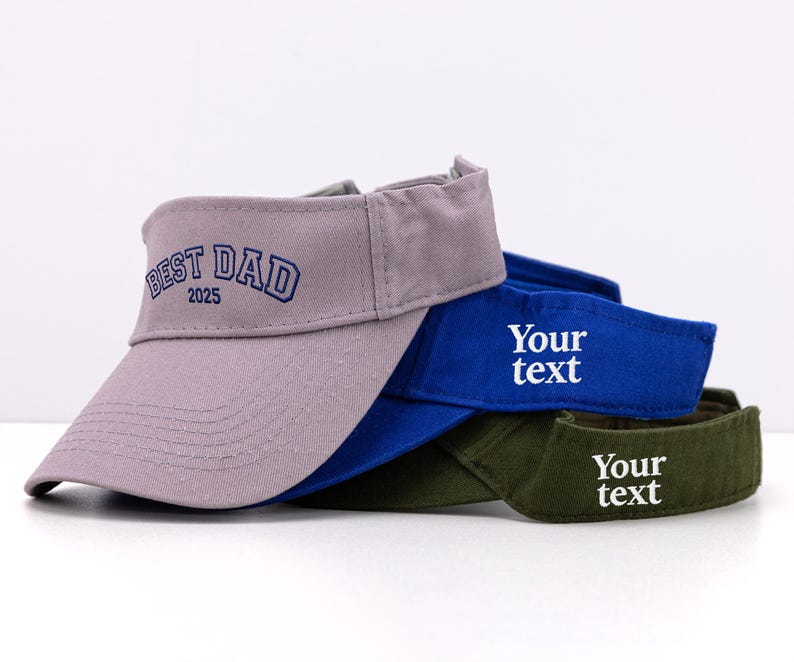K&ouml;nnte beinhalten: Drei Visore in Grau, Blau und Olivgr&uuml;n sind gestapelt. Auf dem grauen Visor ist "BEST DAD 2025" aufgestickt. Die blauen und gr&uuml;nen Visore tragen den Text "Your text" aufgestickt.