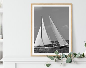 May include: Black and white photograph of two sailboats racing on the water. The sailboats are in the foreground, with the water and sky in the background.