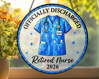 Puede incluir: Un atrapasueños circular de vitral con una casaca médica de patrón de mosaico azul, un estetoscopio, una etiqueta con el nombre Sophia y una botella pequeña. El texto dice OFFICIALLY DISCHARGED, Retired Nurse y 2026, con pequeños signos de más azules.