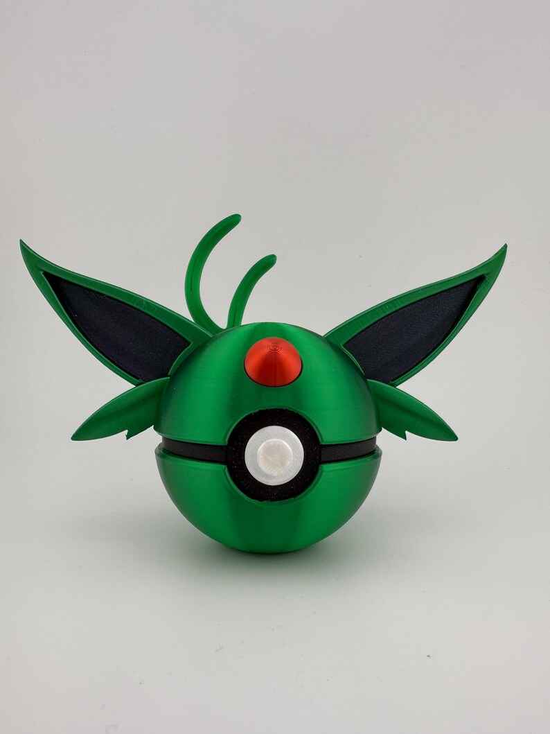 May include: A green and black spherical object with wing-like structures and a red and white circular design. The object has a rounded shape with a segmented design, and is likely a decorative item or toy.